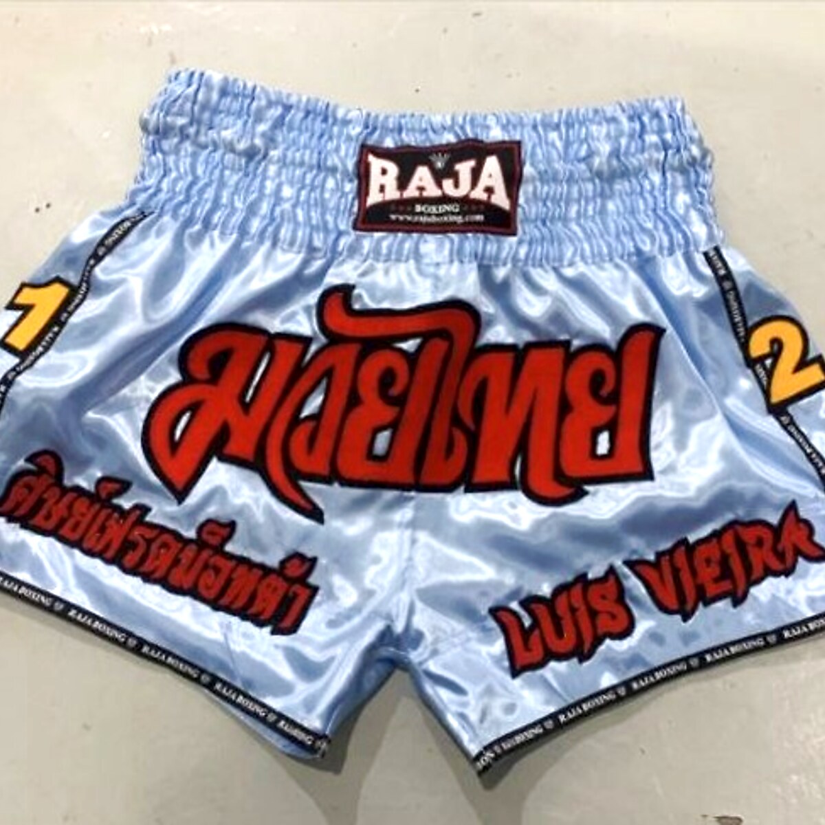 RAJA custom Muay Thai shorts — light blue satin, fighter name embroidery